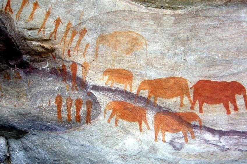 Una pared rocosa con figuras humanas y de animales prehistóricos pintadas en naranja y marrón. 1