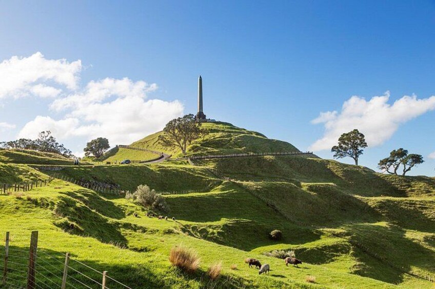 A grassy hill with a monument, sheep grazing, and a clear blue sky. 5