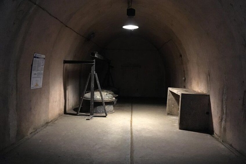 Ein schummrig beleuchteter Tunnel mit einer Metallkonstruktion, einem großen Rad und einer Bank. 2