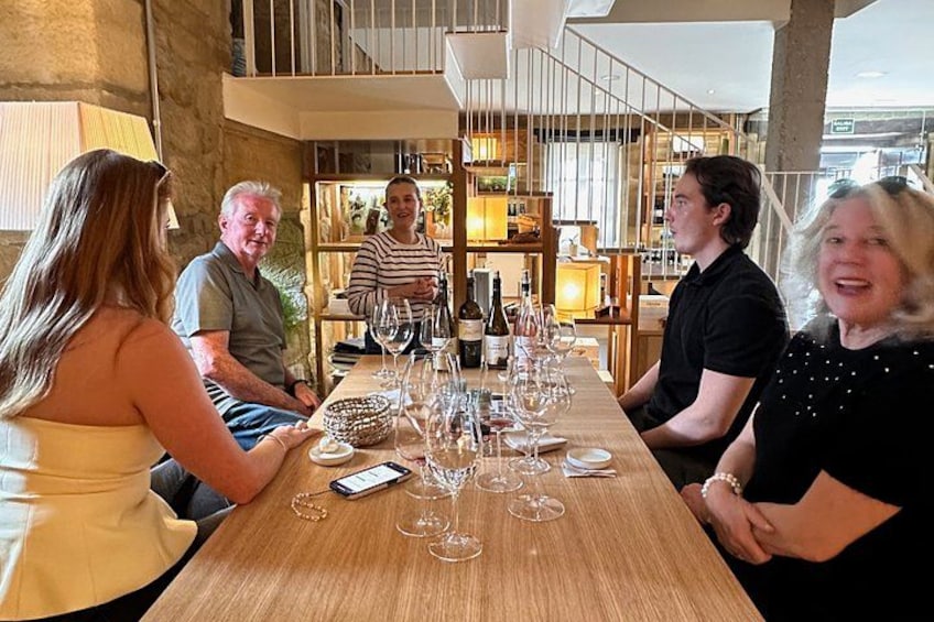 A group of people seated at a wooden table with wine glasses and bottles. 5