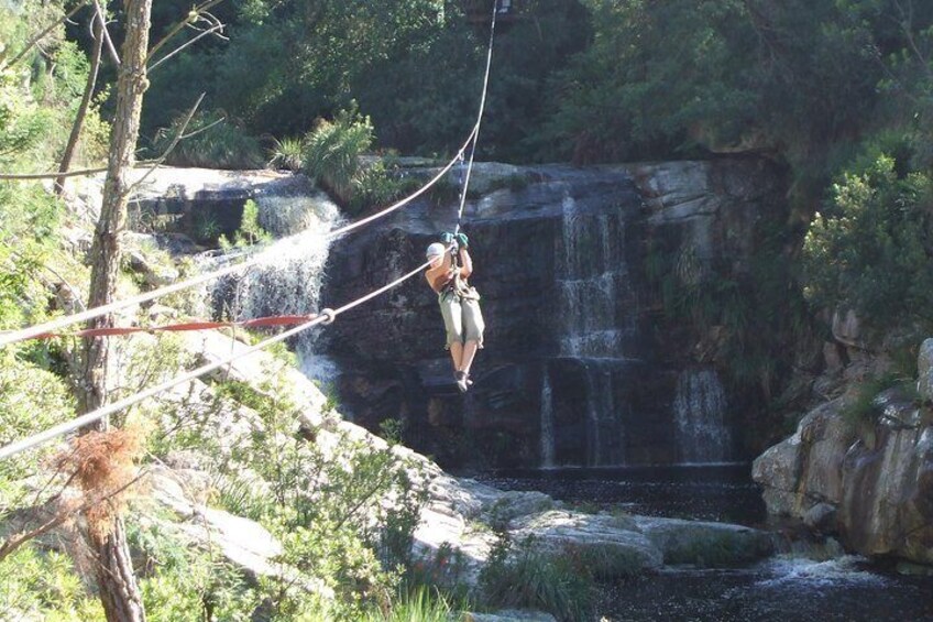 A person zip-lining over a waterfall in a forested area. 5