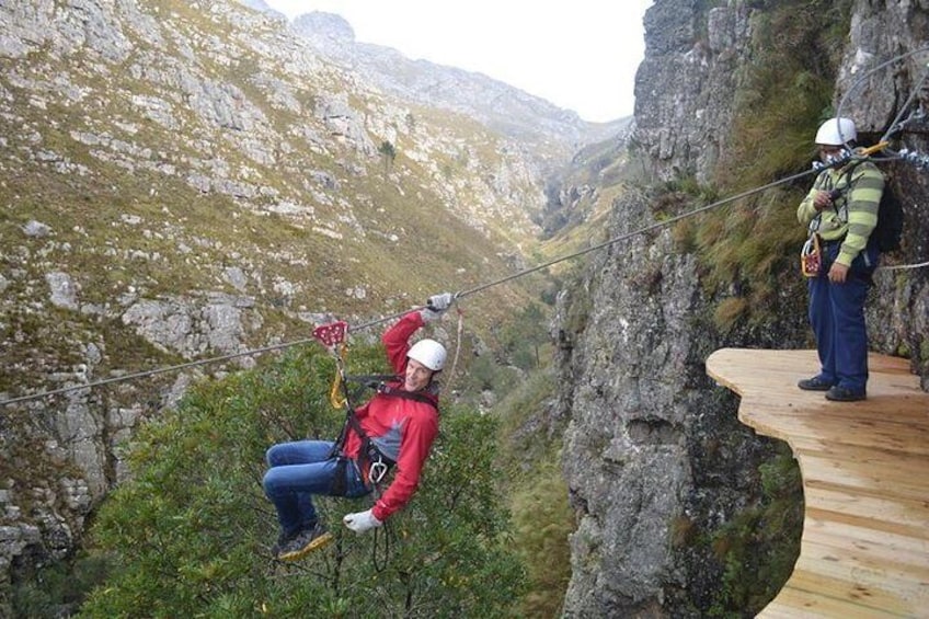 A person rappelling down a rocky cliff with a guide standing on a wooden platform. 1