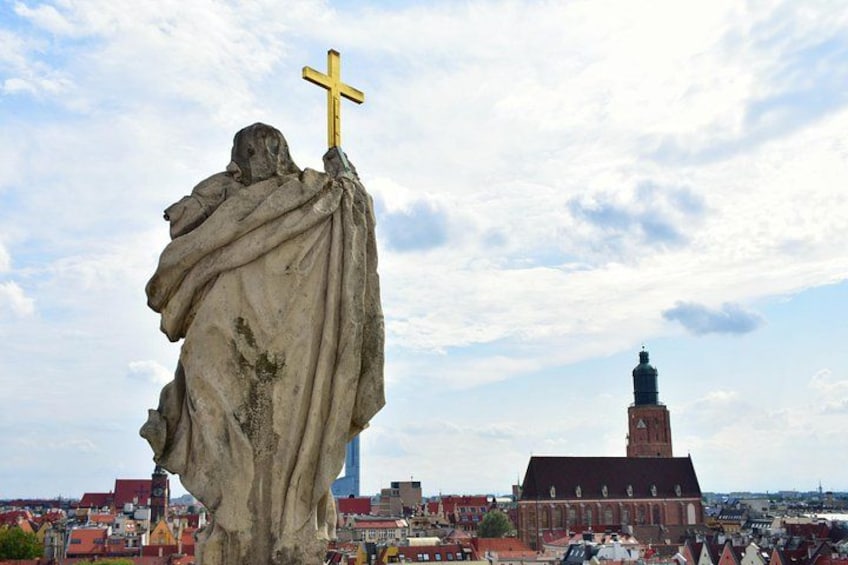 A statue of a figure holding a cross, with a church and a tower in the background. 4