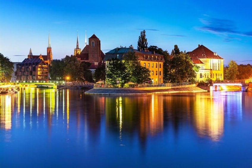 A river with buildings reflecting on the water, a bridge, and a church with spires. 1