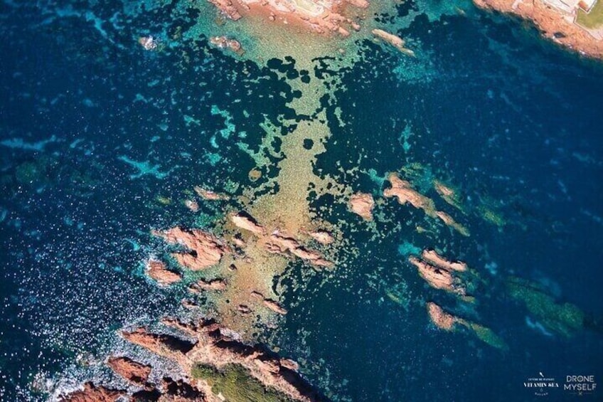 A coastal landscape with clear waters, rocky formations, and a drone watermark. 1