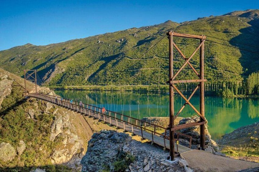 A suspension bridge over a lake with a mountainous backdrop. 1