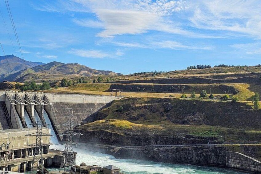 A dam with water flowing over it, surrounded by hills and a clear sky. 4