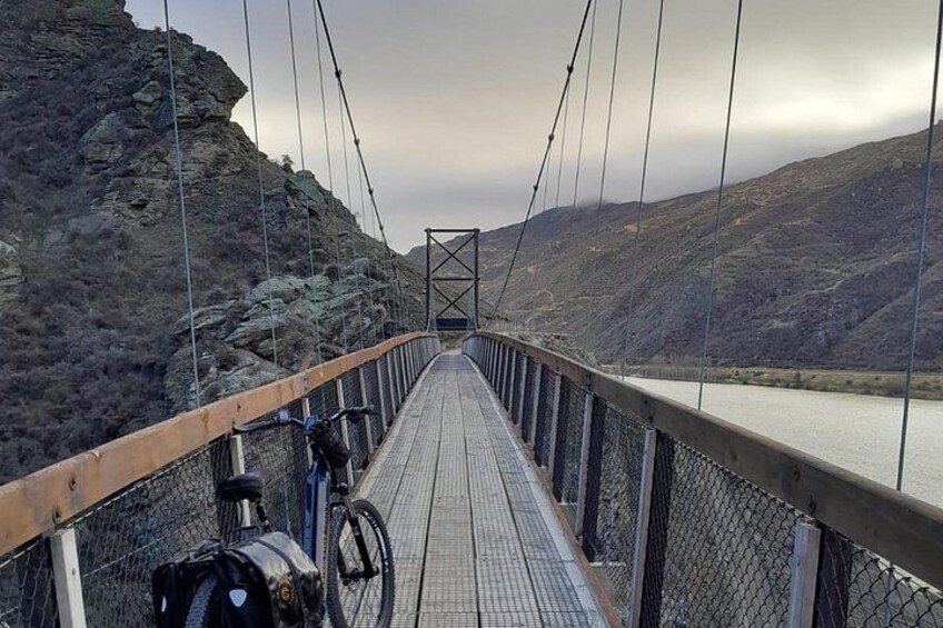 A suspension bridge with a wooden walkway, metal railings, and a rocky landscape in the background. 2