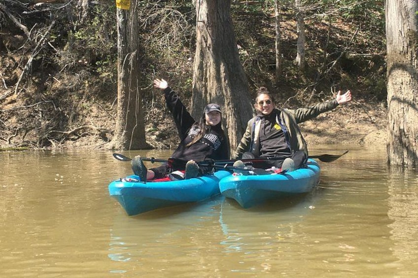 Two people kayaking on a calm river surrounded by trees. 2