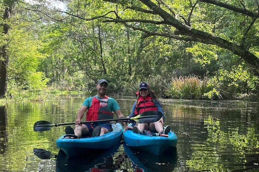Two people kayaking on a calm river surrounded by lush greenery. 4