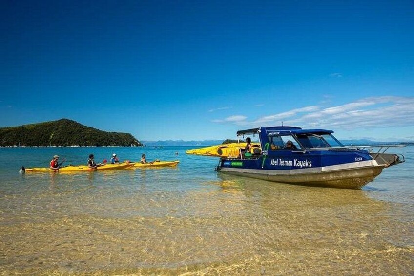 A clear blue sea with kayaks and a boat named 'Ariel Tasman Kayaks' on the shore. 3
