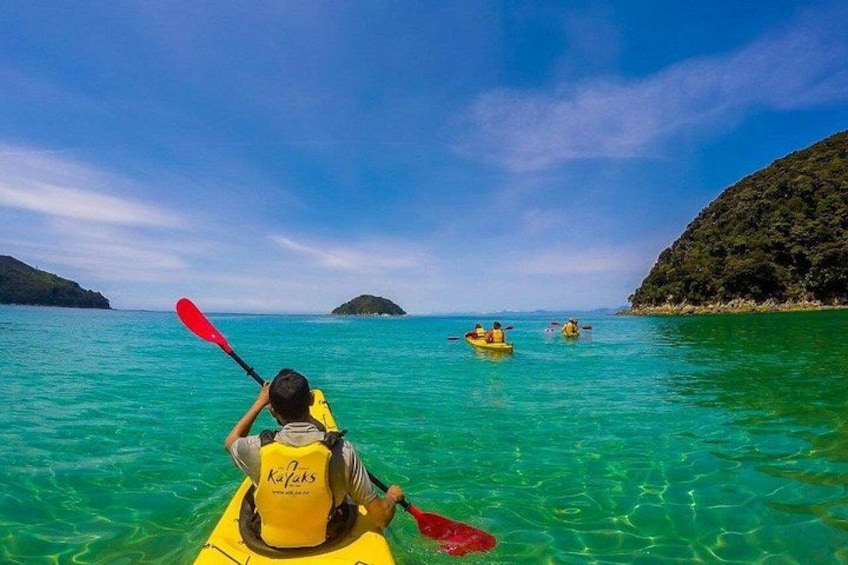 A person kayaking on clear turquoise water with distant islands and a clear sky. 3