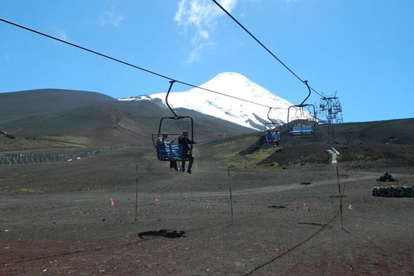 A ski lift with chairs moving towards a snow-capped mountain. 2