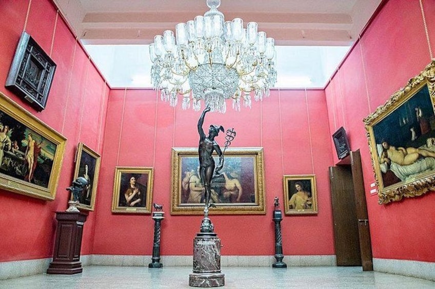 A room with a large chandelier, paintings on the walls, and a statue in the center. 2