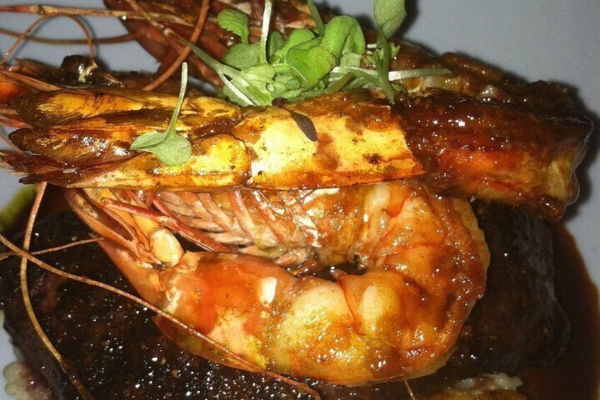 Un plato con camarones y un trozo de carne, adornado con hierbas verdes. 2