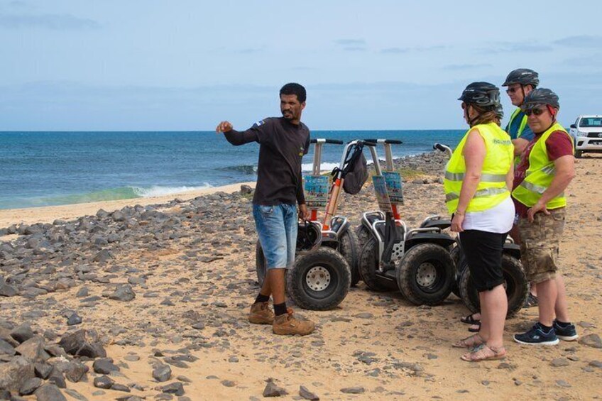 Une plage avec un terrain rocheux, et une personne qui pointe vers l’océan. On peut voir des quads garés sur le sable. 3