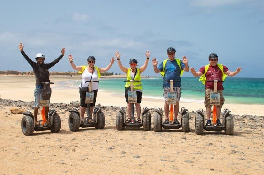 Cinq personnes sur des gyropodes sur une plage de sable, avec l’océan en arrière-plan. 1