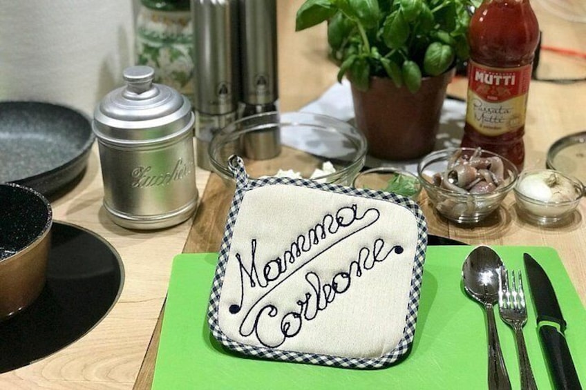A kitchen counter with a checkered cloth, a green cutting board, a metal container, a bottle of ketchup, and a plant. 1
