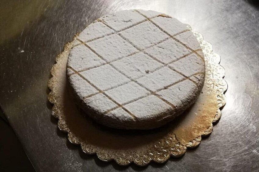 A round cake with a crisscross pattern on top, placed on a decorative doily. 3