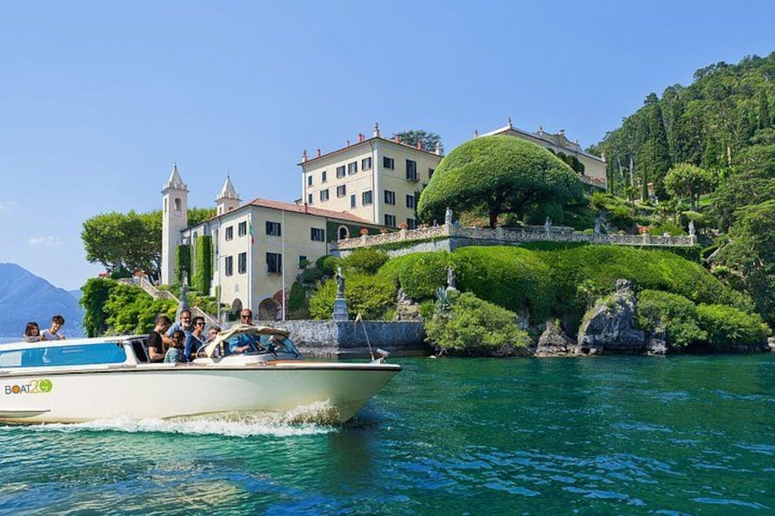 A boat with passengers, a large building with a tower, and lush greenery on a hillside. 1