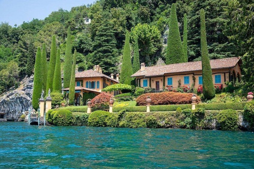 A lake with a house surrounded by tall trees and well-maintained gardens. 4