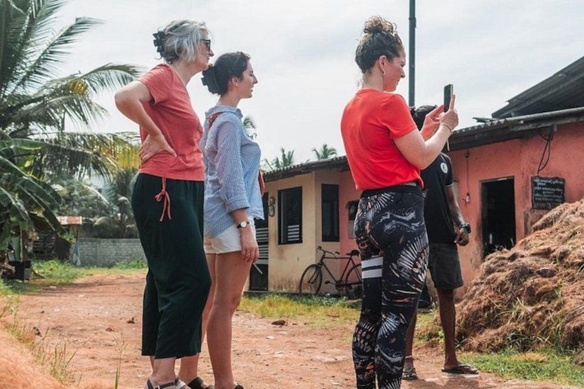 Four people standing outdoors, a dirt path, a building, and a bicycle. 3