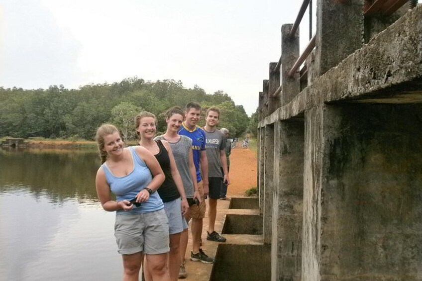 A group of people standing on a concrete bridge over a body of water, with trees in the background. 2