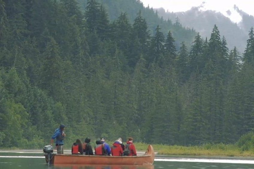 A group of people in a boat on a river, surrounded by dense forest. 5