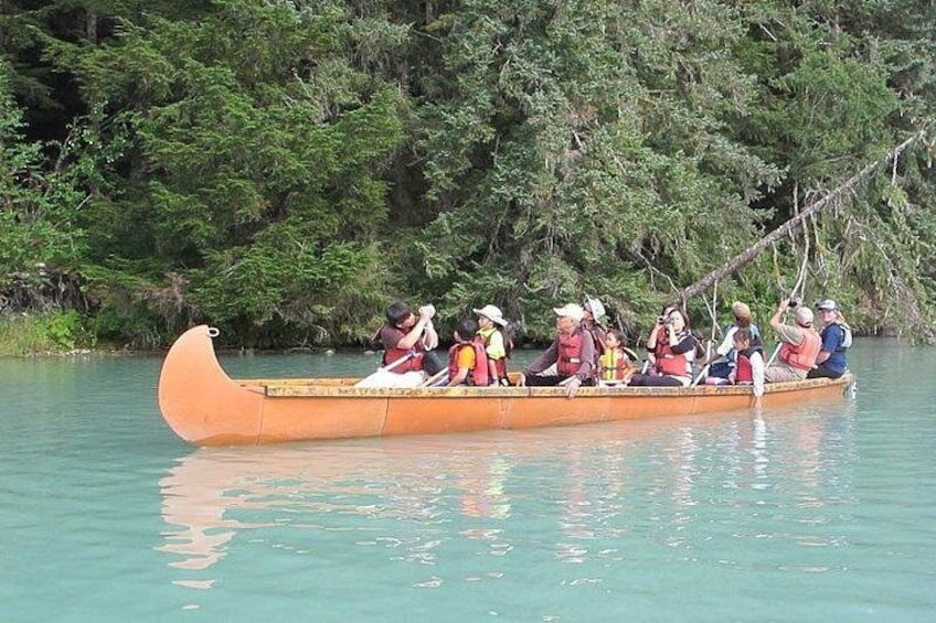 A group of people in a longboat on calm water, surrounded by dense greenery. 1