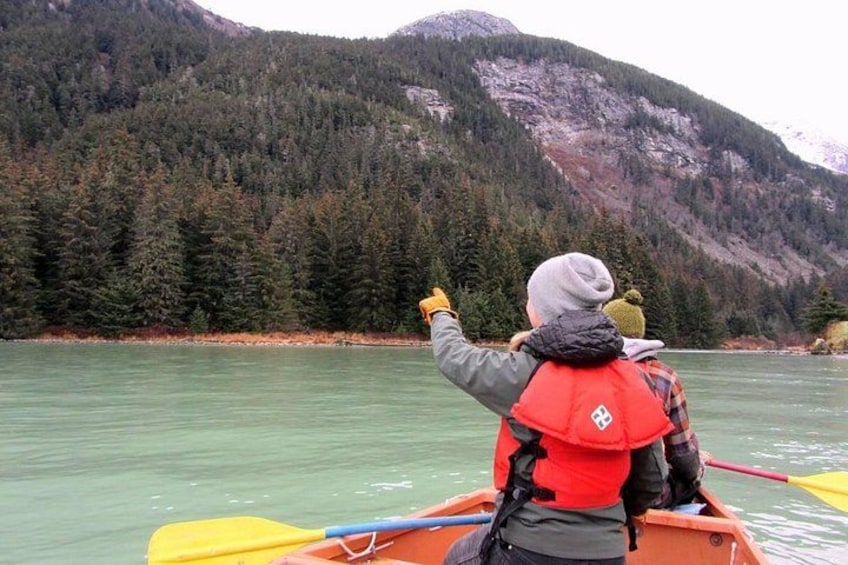 Two people in a canoe on a calm river, surrounded by dense forest and mountains. 3