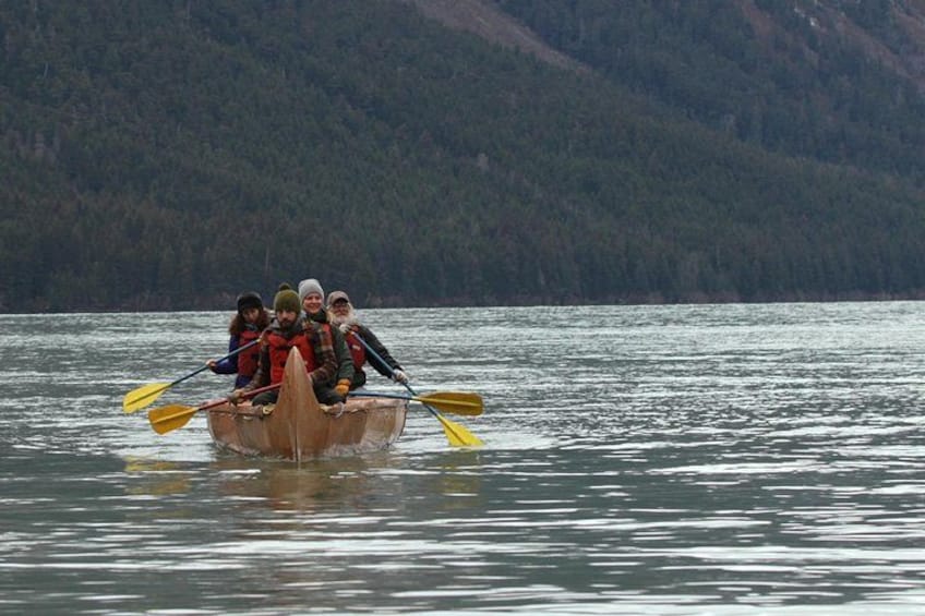 A group of people in a wooden boat on a calm lake with mountains in the background. 4