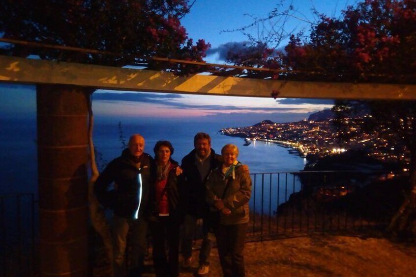 A group of people standing under a pergola with a coastal view at dusk. 2