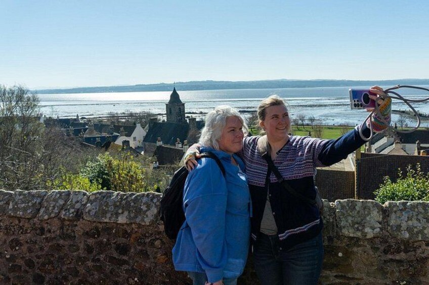Två personer som tar en selfie med en vacker utsikt över en stad och en sjö eller ett annat vattendrag i bakgrunden. 2