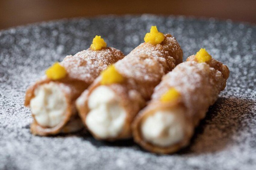 Trois cannolis saupoudrés de sucre glace et décorés de petits motifs jaunes, présentés sur une assiette à texture. 3
