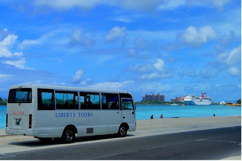 Een witte bus met de tekst 'Liberty Tours' staat langs de waterkant, met een cruiseschip op de achtergrond. 4