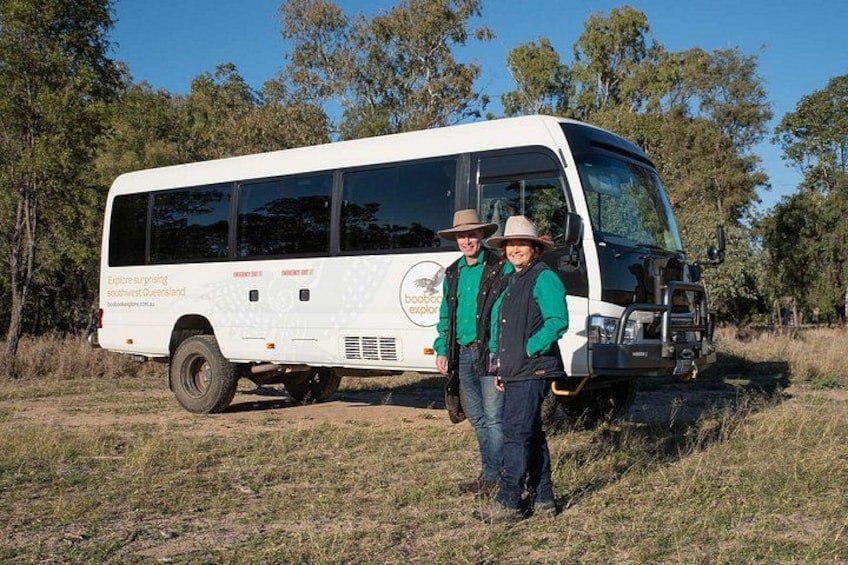 Un autobus blanc avec l’inscription « Découvrez les merveilles du Queensland », deux personnes debout devant, et un paysage boisé en arrière-plan. 3
