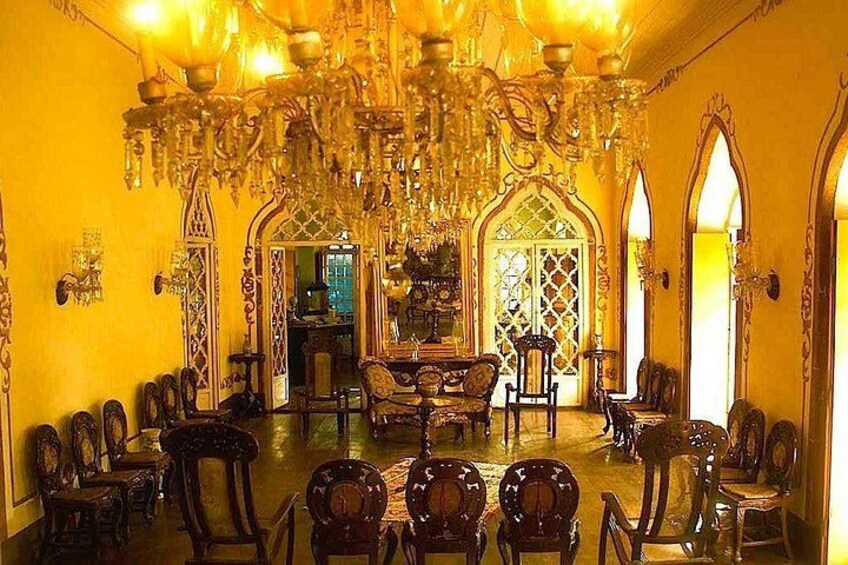 An ornate room with chandeliers, wooden chairs, and a mirror. 5