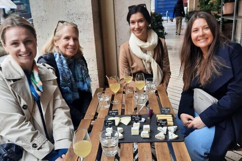 Quatre personnes sont assises autour d’une table en bois, à l’extérieur, devant des verres de vin et des assiettes de fromage. 3