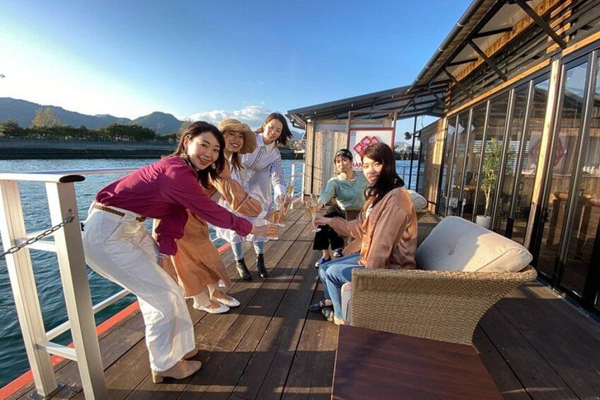 A group of people on a wooden deck by a body of water with mountains in the background. 1