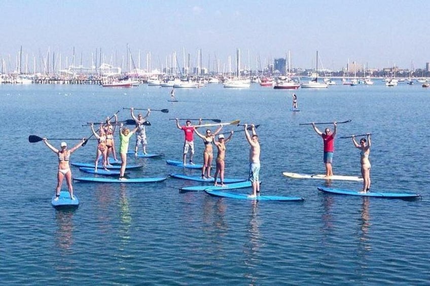 Des personnes pratiquent le paddle sur une mer calme, avec une marina en arrière-plan. 1