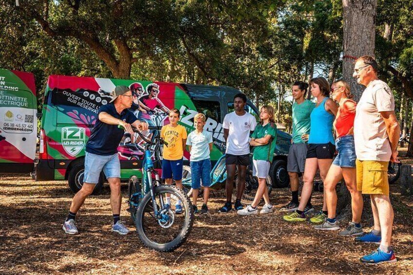 A group of people around a bicycle in a park with trees and a colorful bus in the background. 1