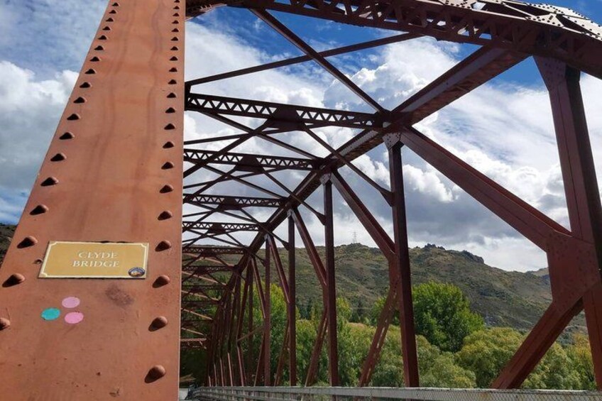 A metal bridge with a sign reading 'Clyde Bridge' against a backdrop of hills and a partly cloudy sky. 2