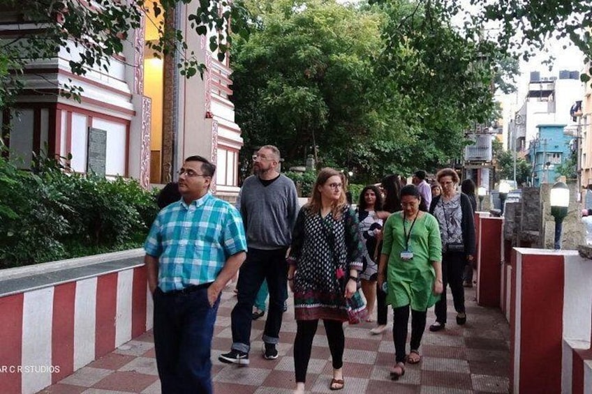 A group of people walking on a red and white checkered pavement, surrounded by greenery and buildings. 5