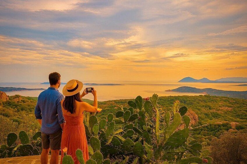 Una pareja fotografiando un atardecer sobre un paisaje costero con cactus y montañas al fondo. 4