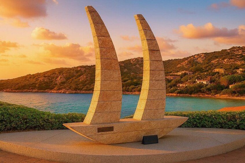 Una escultura moderna con tres elementos curvos, frente a un paisaje costero con colinas y una masa de agua al atardecer. 5