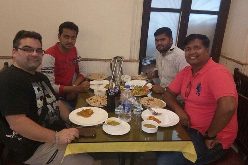Four people seated around a table with plates of food, bottles, and a water dispenser. 2