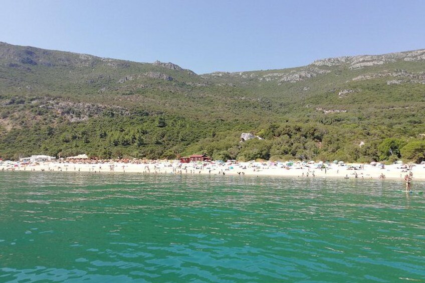 Una spiaggia con persone, acqua cristallina e colline verdi sullo sfondo. 2