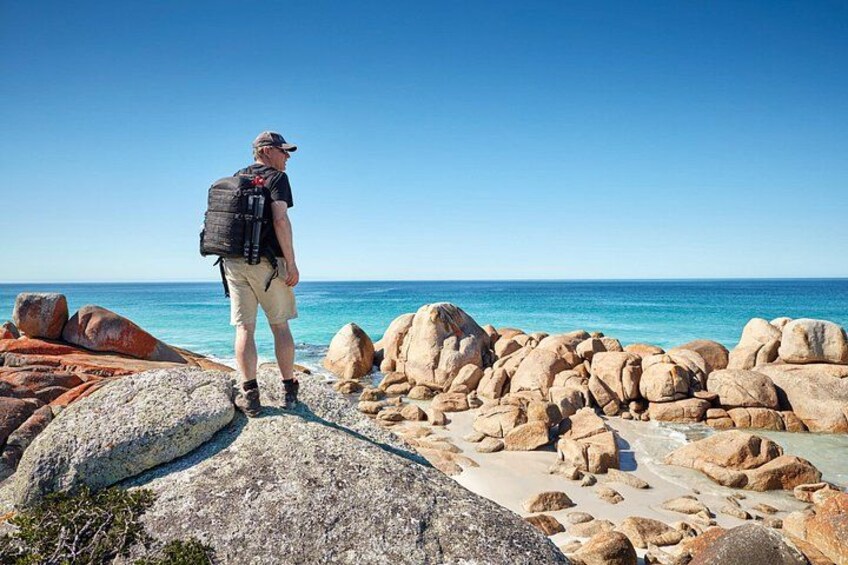 En person som står på en stenstrand med stora stenblock och havet i bakgrunden. 2