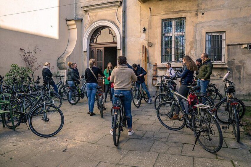 Een groep mensen staat voor een gebouw, met fietsen geparkeerd in de buurt. 3