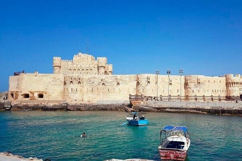 A historic stone fortress by a clear blue sea with two boats. 1